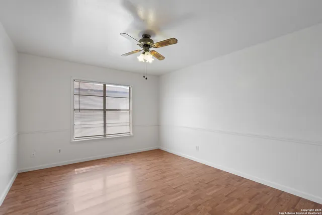 an empty room with wooden floor fan and windows