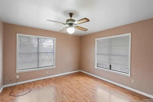 an empty room with wooden floor fan and windows