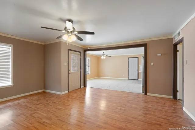 a view of an empty room with wooden floor and a ceiling fan