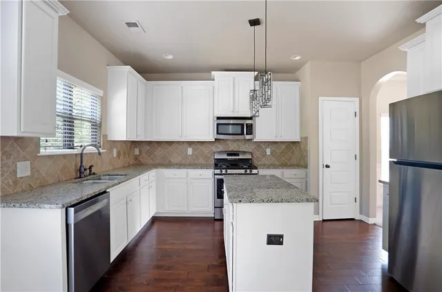 a kitchen with stainless steel appliances granite countertop a refrigerator a sink dishwasher a stove and white cabinets with wooden floor