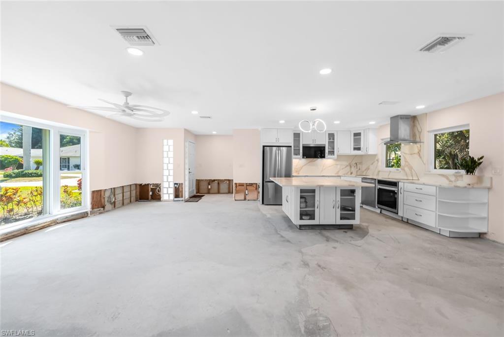 24 Rivard Road, Unit 12 Naples, FL 34112 - Photo 8 of 27 Kitchen featuring appliances with stainless steel finishes, a wealth of natural light, white cabinets, a center island, and wall chimney exhaust hood