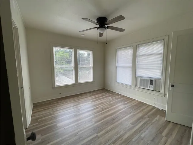 an empty room with wooden floor chandelier fan and windows