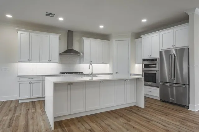 a kitchen with stainless steel appliances a stove top oven a sink a refrigerator and white cabinets