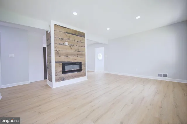 a view of an empty room with wooden floor fireplace and a window