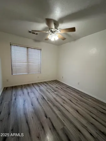 an empty room with wooden floor chandelier fan and windows