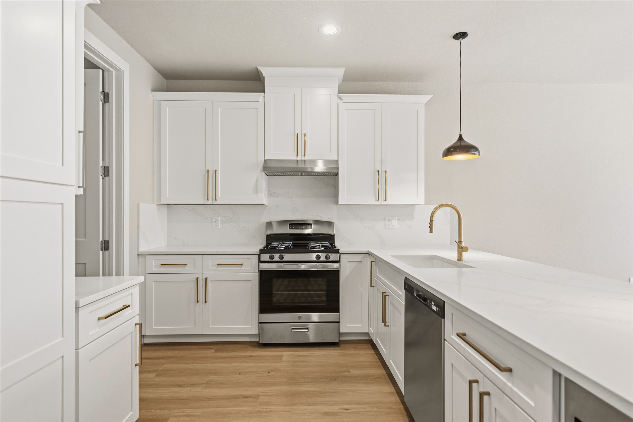 3422 Elser Street Houston, TX 77009 - Photo 7 of 26 This modern kitchen features sleek white cabinetry with gold handles, a stainless steel gas stove and dishwasher, and elegant quartz countertops. A stylish pendant light and wooden flooring add warmth and sophistication.