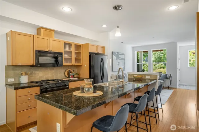 a kitchen with stainless steel appliances granite countertop a stove a sink a microwave a dining table and chairs with wooden floor