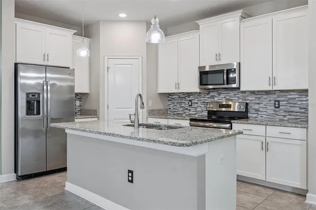 a kitchen with stainless steel appliances granite countertop a sink a stove a refrigerator a microwave a sink and white cabinets