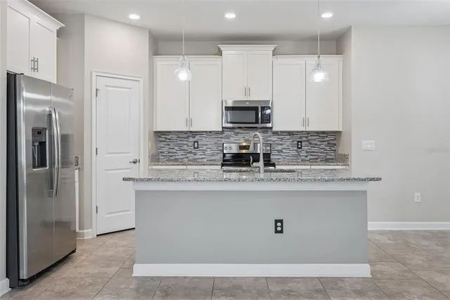 a kitchen with stainless steel appliances granite countertop a refrigerator a stove a sink and white cabinets