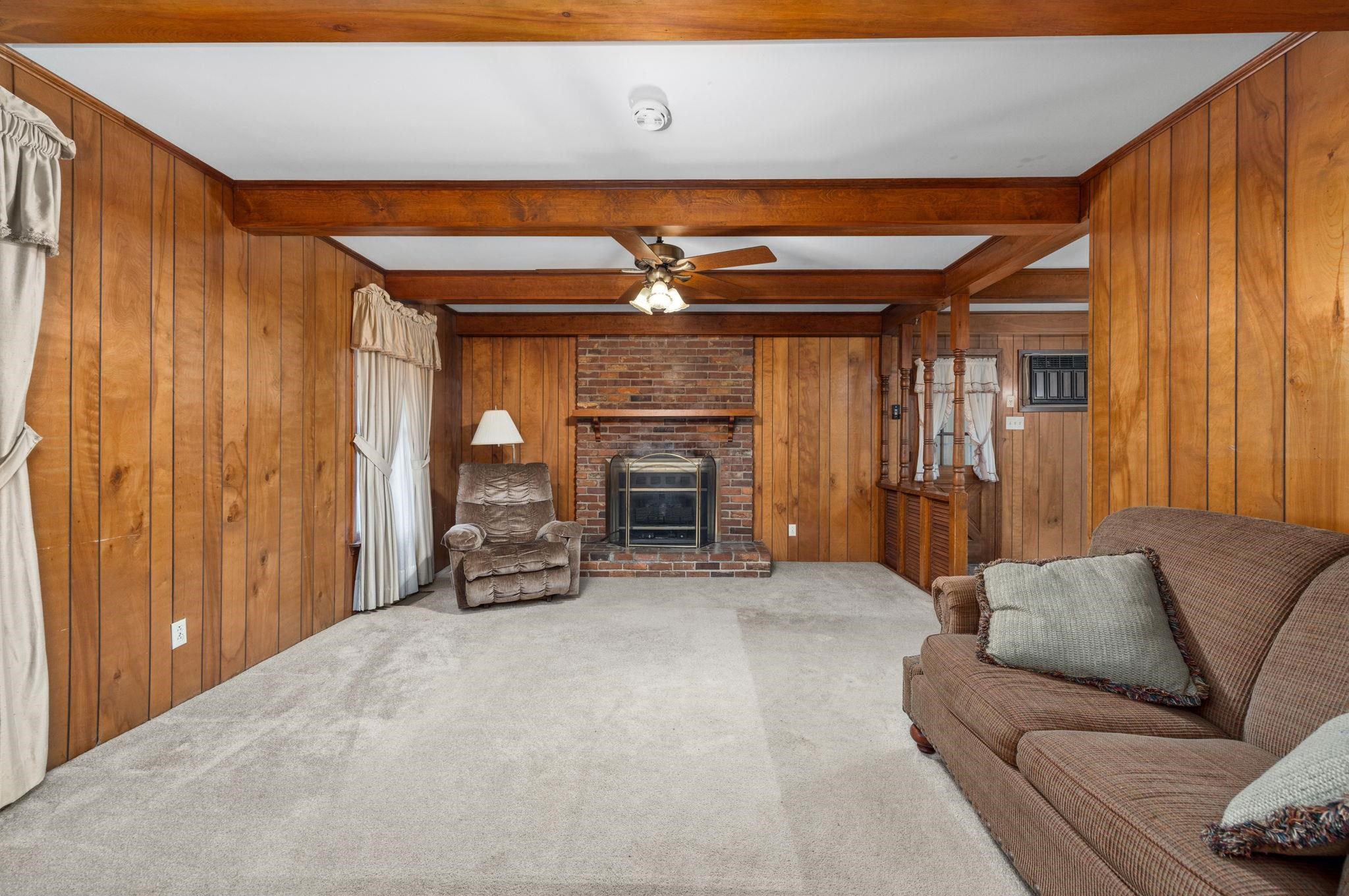 213 Forrest School Road Corinth, MS 38834 - Photo 6 of 40 Living room featuring beam ceiling, ceiling fan, carpet floors, wooden walls, and a fireplace