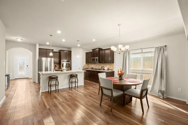 a kitchen with stainless steel appliances granite countertop a stove top oven a sink dishwasher a dining table and chairs with wooden floor