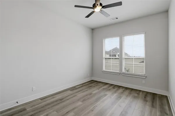an empty room with wooden floor fan and windows