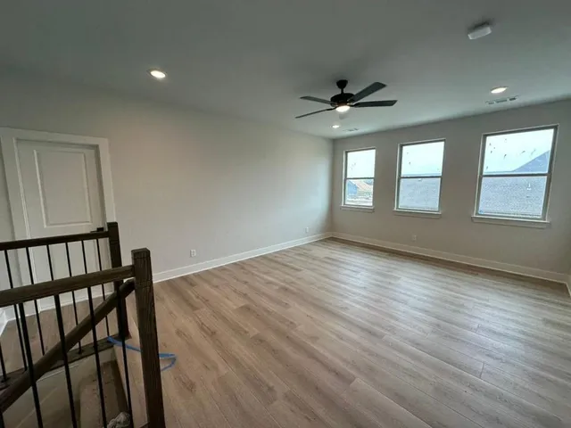 an empty room with wooden floor chandelier fan and windows