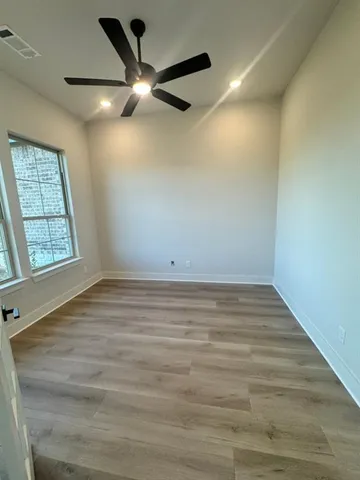 an empty room with wooden floor fan and windows
