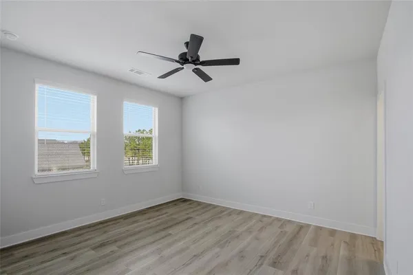an empty room with wooden floor fan and windows