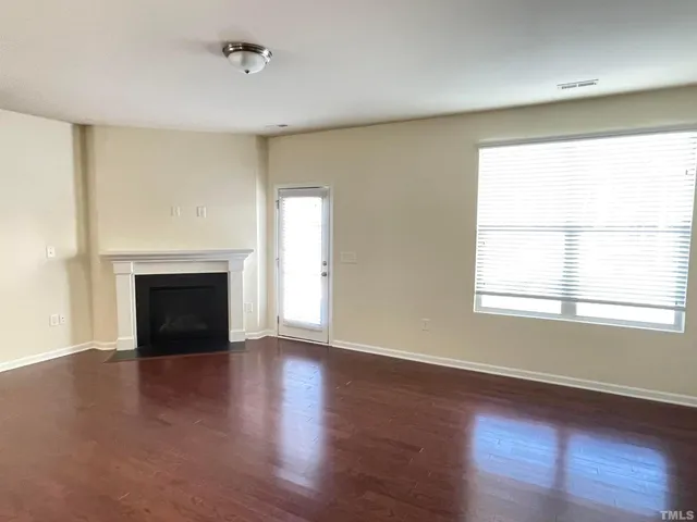 an empty room with wooden floor fireplace and windows