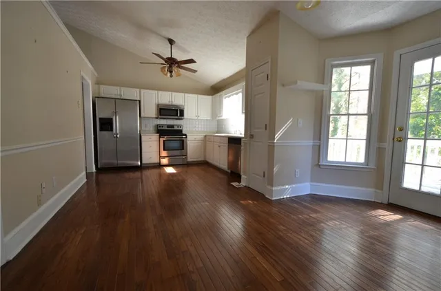 an empty room with wooden floor steel appliances and windows