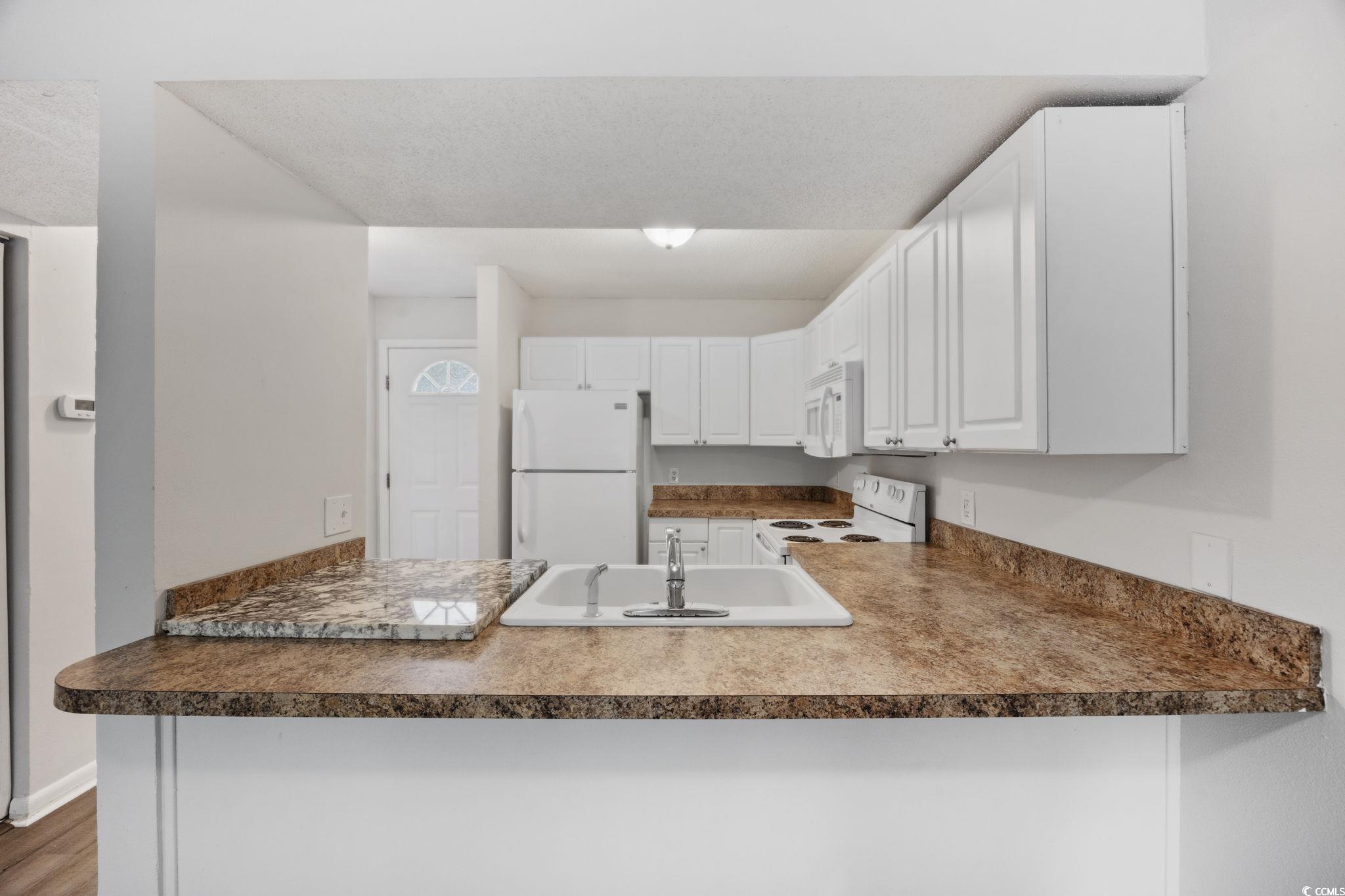 3555 Highway 544, Unit 8H Conway, SC 29526 - Photo 6 of 22 Kitchen featuring white appliances, a peninsula, white cabinets, dark countertops, and wood finished floors
