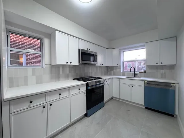 a kitchen with white cabinets appliances a sink and a window