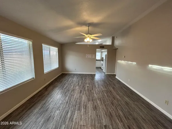 an empty room with wooden floor chandelier fan and windows