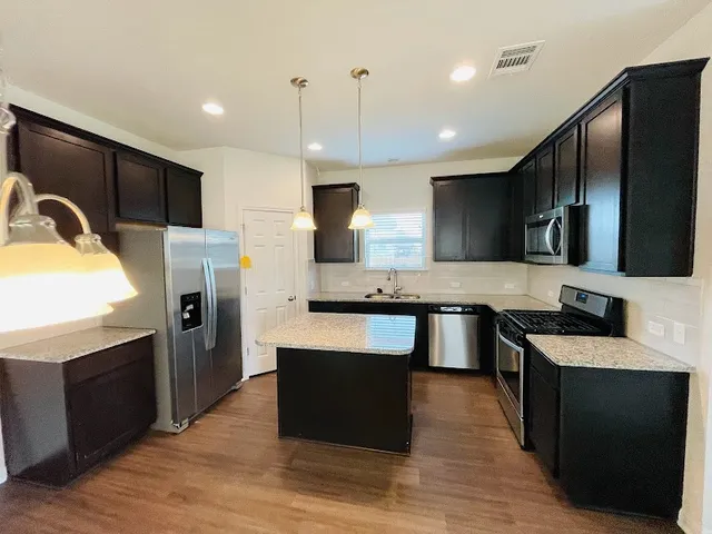 a large kitchen with stainless steel appliances wooden cabinets a refrigerator and a stove top oven