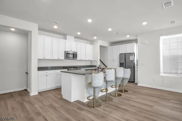 a kitchen with stainless steel appliances granite countertop a stove a sink a refrigerator and white cabinets with wooden floor