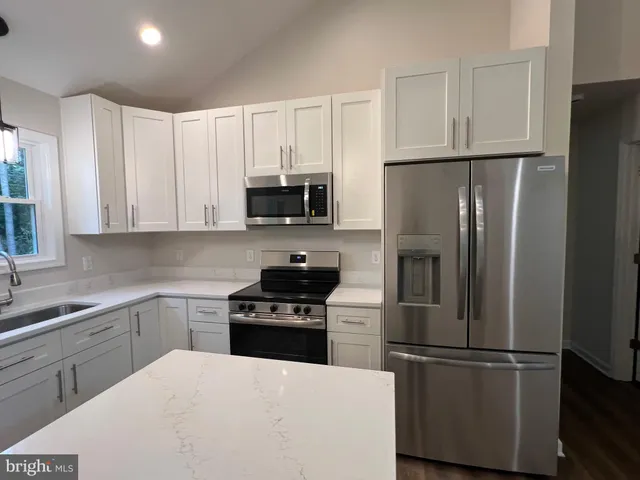 an empty room with wooden floor and kitchen view