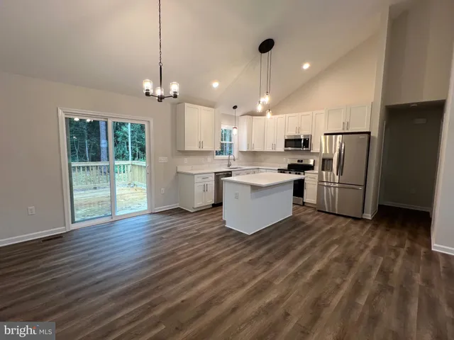 a view of an empty room with wooden floor and a kitchen space