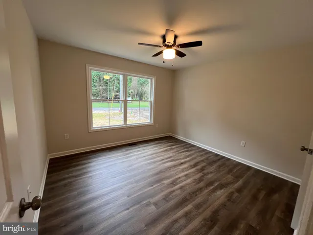an empty room with wooden floor ceiling fan and windows