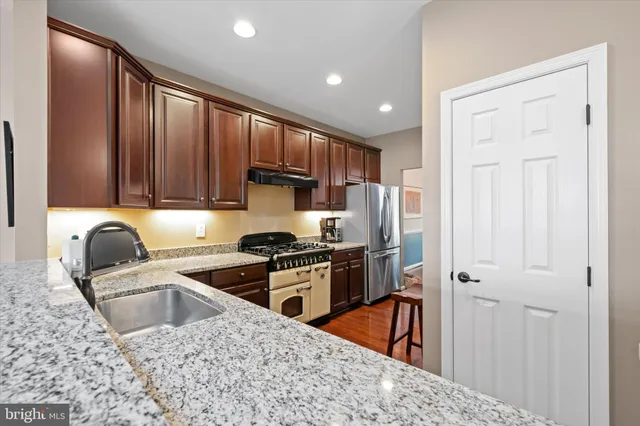 a kitchen with granite countertop wooden floors wooden cabinets and stainless steel appliances