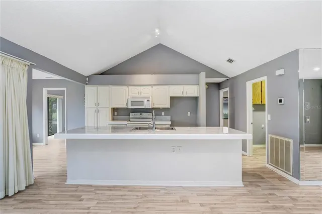 a large white kitchen with kitchen island a sink a center island and stainless steel appliances