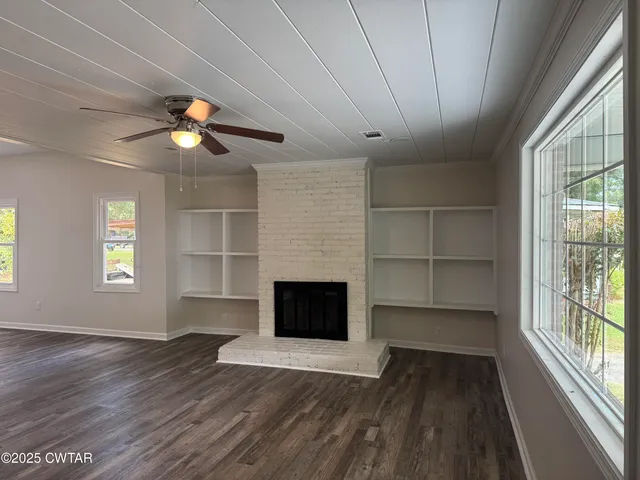 an empty room with wooden floor chandelier fan and windows