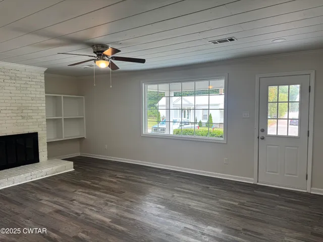 an empty room with windows fireplace and a kitchen view
