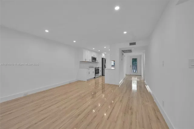 a view of empty room with wooden floor and kitchen