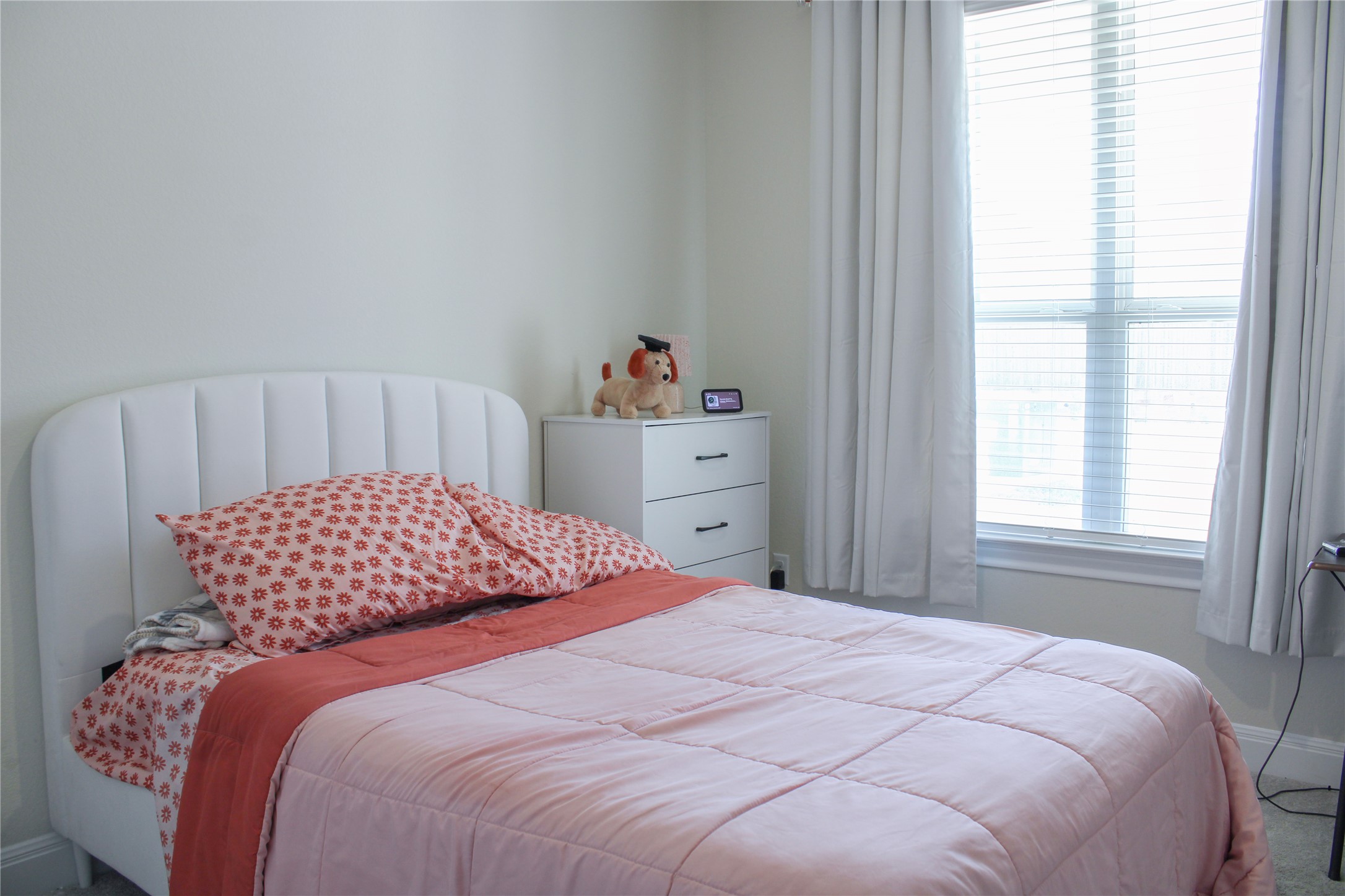 A tall window lets natural light wash over carpeted flooring in this tranquil bedroom.