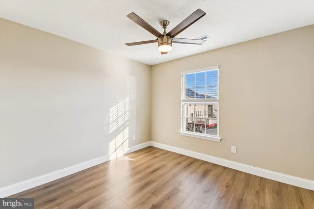 an empty room with wooden floor ceiling fan and windows