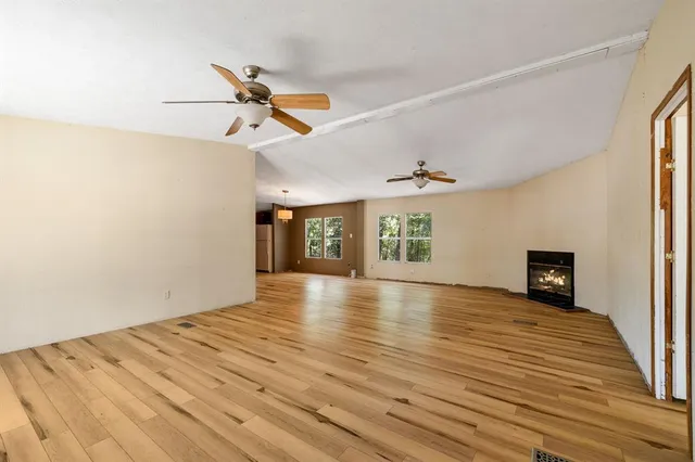 an empty room with wooden floor ceiling fan and windows