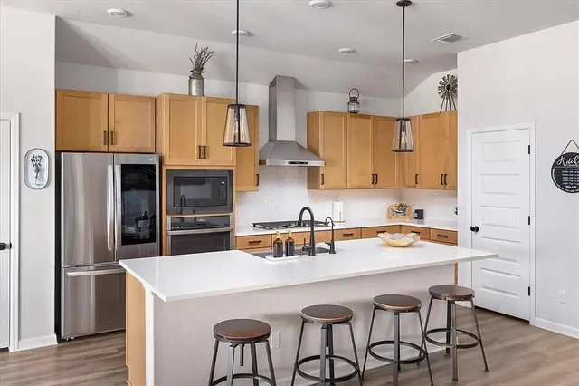 a kitchen with stainless steel appliances a stove a sink a refrigerator and chairs with wooden floor