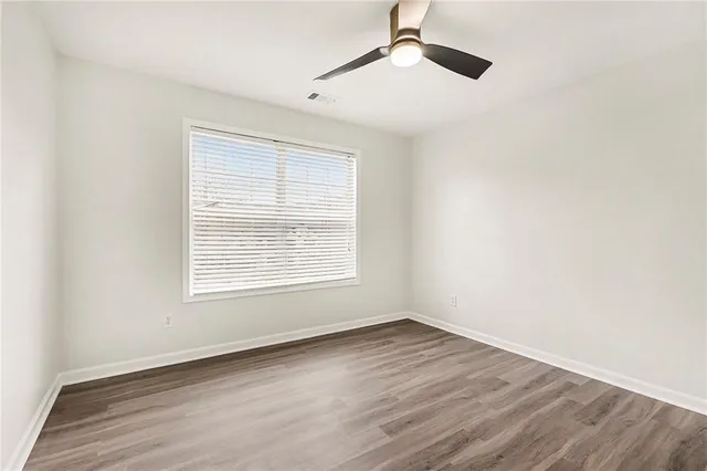 an empty room with wooden floor ceiling fan and windows