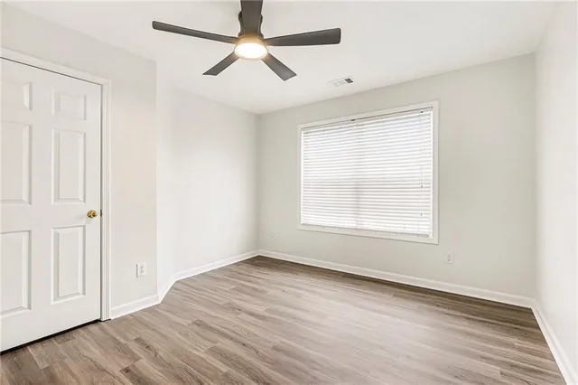 an empty room with wooden floor ceiling fan and windows