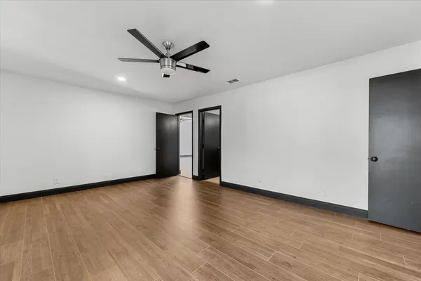 a view of an empty room with wooden floor and a ceiling fan