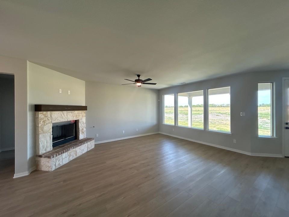 8685 County Road 623 Blue Ridge, TX 75424 - Photo 5 of 12 Spacious room featuring wood-finish flooring, a stone-clad fireplace with a hearth, multiple windows, and a ceiling fan