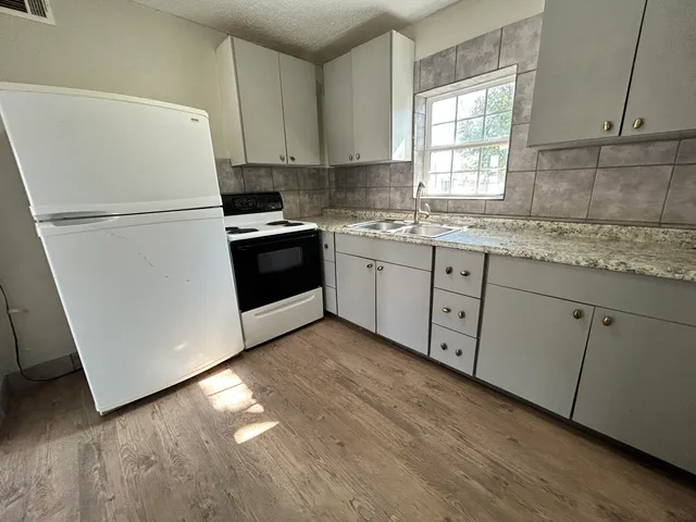 a kitchen with granite countertop white cabinets white appliances a sink and a window