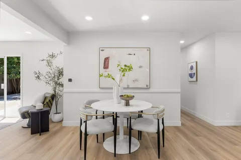 a kitchen with stainless steel appliances kitchen island granite countertop a stove a refrigerator a sink a dining table and chairs with wooden floor