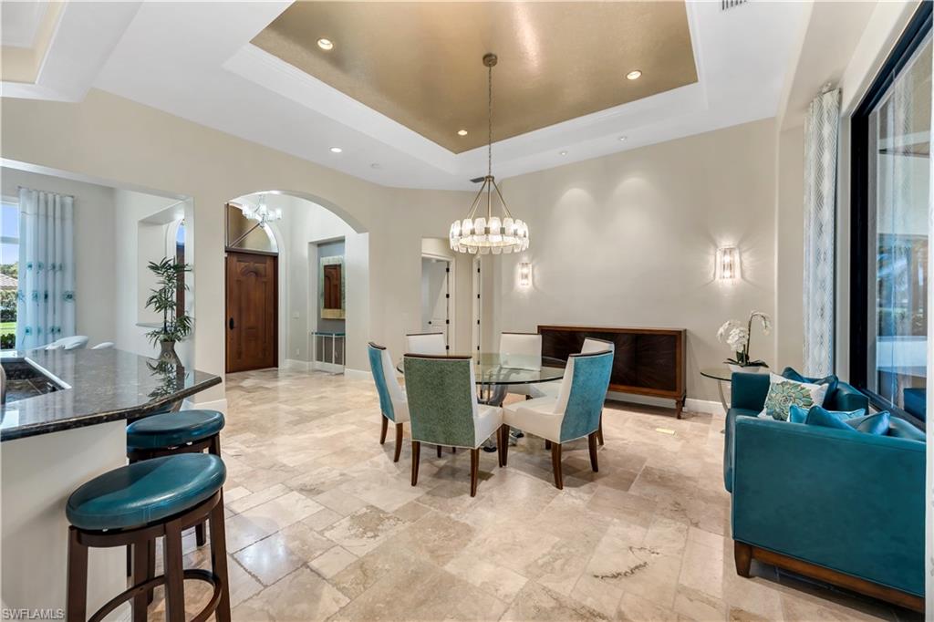 11875 Hedgestone Court Naples, FL 34120 - Photo 7 of 29 Tray ceiling with gold-finish accent, textured tile flooring, built-in counter with dark countertop, large sliding glass door, and arched doorway