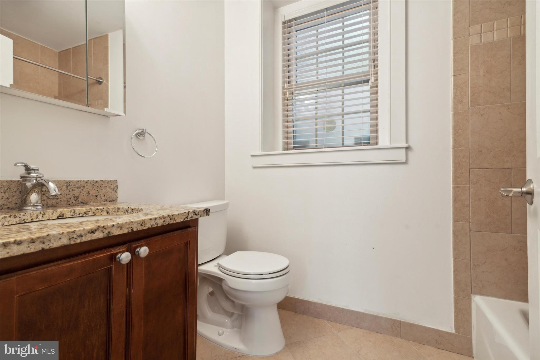 4300 Spruce Street, Unit A101 Philadelphia, PA 19104 - Photo 17 of 25 a bathroom with a granite countertop toilet a sink and a window