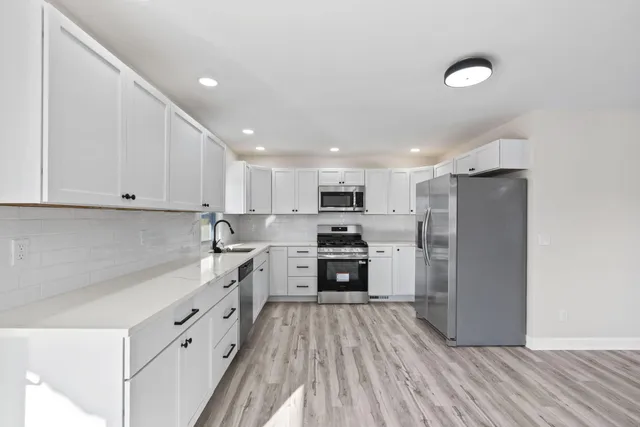 a kitchen with stainless steel appliances granite countertop a refrigerator a stove top oven a sink and dishwasher with wooden floor