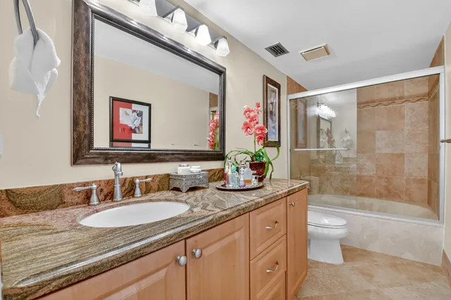 a bathroom with a granite countertop sink a toilet a mirror a vanity a shower and bathtub
