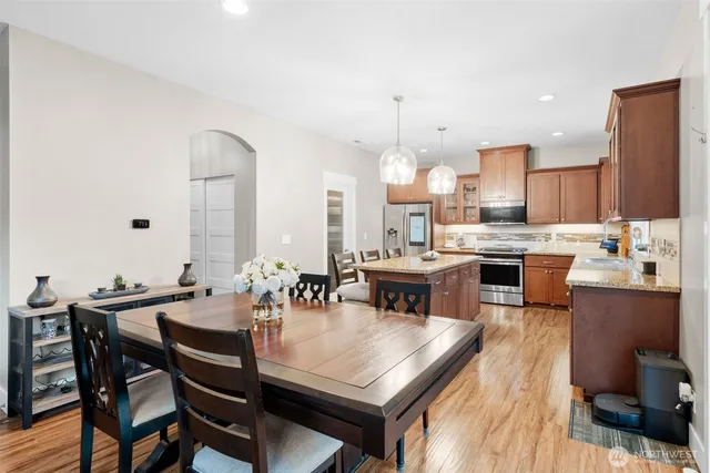 a open dining room with stainless steel appliances kitchen island granite countertop a table chairs and a oven
