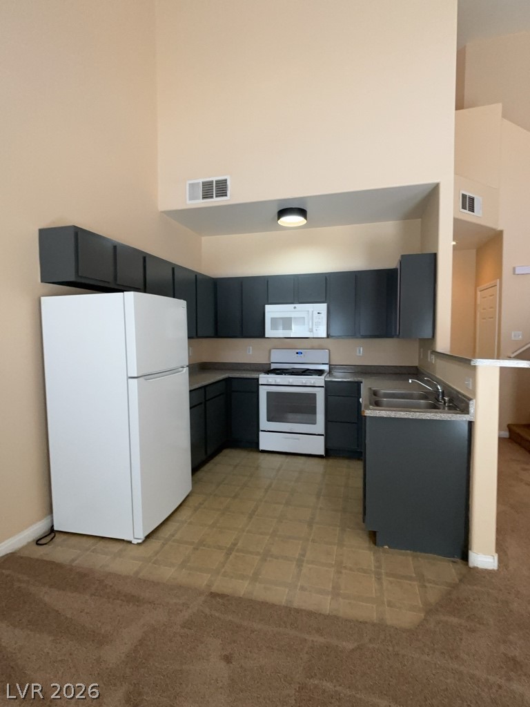 4915 East Russell Road, Unit 145 Las Vegas, NV 89120 - Photo 4 of 13 Kitchen with white appliances, a high ceiling, light colored carpet, a peninsula, and dark cabinetry